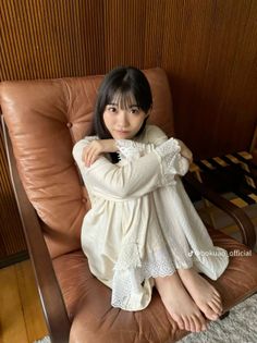 Young woman with long hair and bangs sitting on a brown chair in a white dress