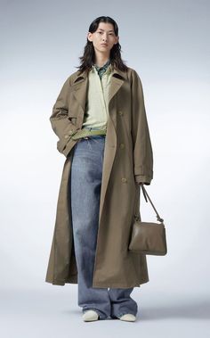Person in a trench coat, green shirt, and wide leg jeans holding a shoulder bag