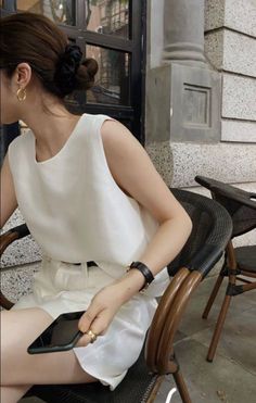Woman in a white top and shorts with hair in a bun, sitting outdoors
