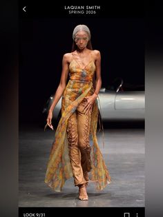 Model on a runway wearing a long sheer dress over lace-up pants