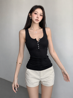 Woman in a black tank top and white shorts posing indoors