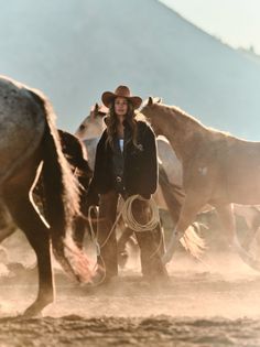 Cowgirl in a cowboy hat holding a lasso among horses in a dusty outdoor setting