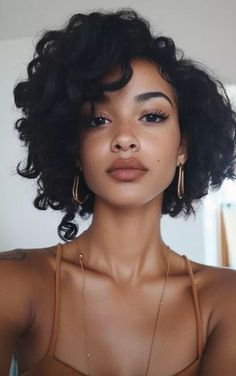 Woman with short curly hair and gold jewelry looking directly at the camera
