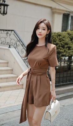 Woman in a brown romper holding a white handbag outdoors