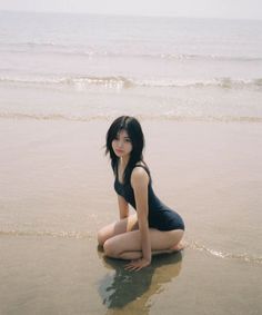 Woman in a black swimsuit kneeling on wet sand at the beach