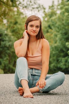 Young woman with long hair sitting outdoors in a pink tank top and blue jeans