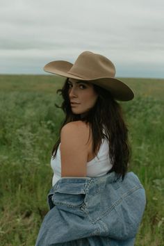 Woman in a cowboy hat and denim jacket in a green field under an overcast sky