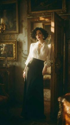 Woman in a white blouse and long skirt leaning against a doorway with dramatic lighting