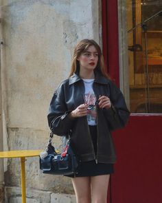 Woman in a leather jacket and mini skirt holding sunglasses outdoors