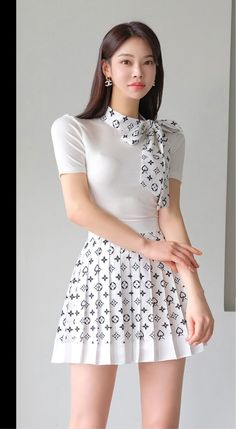 Woman with long hair wearing a white top and pleated short skirt indoors