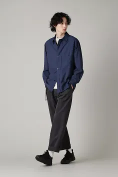 Man in a navy blue shirt and black pants with curly hair in a studio