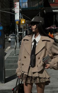 Woman in a beige jacket, pleated skirt, and baseball cap on a city street