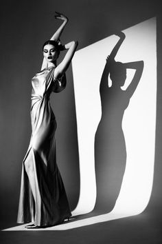 Woman in a long dress with arms raised, casting a dramatic shadow