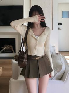 Woman in a pleated skirt and cardigan covering her face with her hand indoors