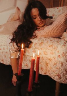 Woman with long dark hair resting on a bed with lit red candles in the foreground