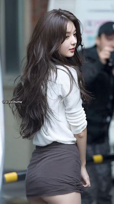 Woman with long dark hair wearing a white top and mini skirt outdoors