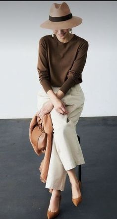 Woman in a brown top and white pants with a wide brim hat and small handbag