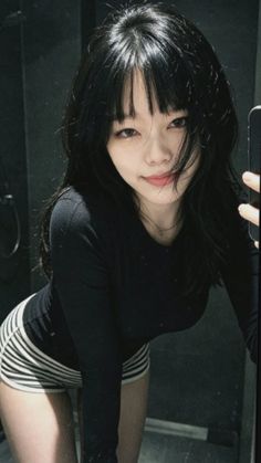 Woman with long black hair and bangs in a black long sleeve shirt and striped shorts