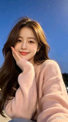 Woman with long brown hair wearing a pink sweater, smiling outdoors