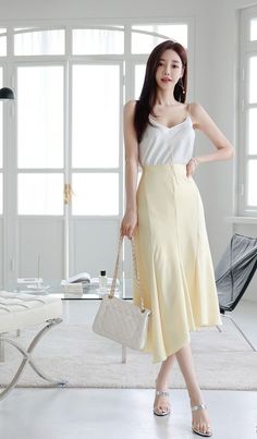 Woman in a white camisole and yellow skirt holding a quilted handbag indoors
