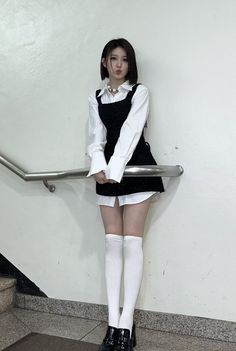Woman with short hair in a black dress and white shirt, holding a handrail