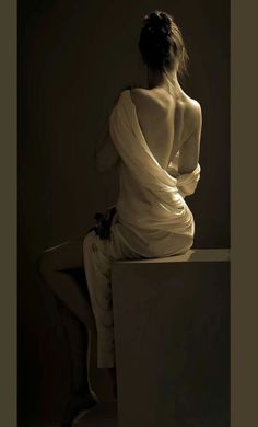 Woman with exposed back draped in fabric, sitting in dramatic lighting