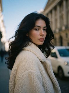 Woman with long dark hair wearing a cream coat on a city street
