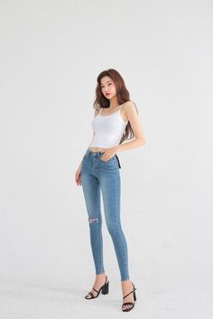 Woman in a white tank top and skinny jeans posing against a white background