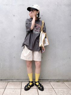 Person in an oversized t-shirt, shorts, and yellow socks against a concrete wall
