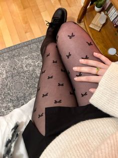 Person wearing black tights with bow patterns, black boots, and a sweater