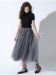 Woman in a black turtleneck top and a gray tulle skirt posing in a studio