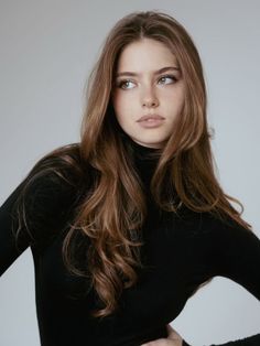 Woman with long brown hair and freckles wearing a black turtleneck in a studio