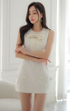 Woman in a white dress with a pearl necklace and bow, posing indoors