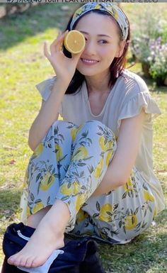 Woman in lemon print pants and a headband holding a lemon slice over her eye