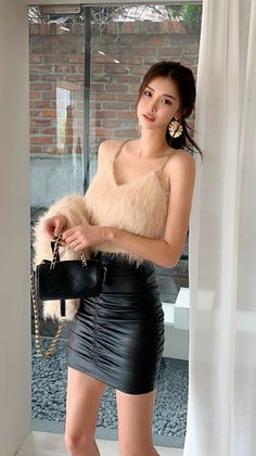 Woman in a furry top and black mini skirt holding a handbag indoors