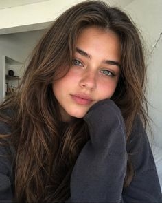 Young woman with long brown hair and green eyes resting her chin on her hand