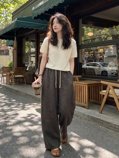 Woman with long hair in wide leg pants walking on a street past a cafe