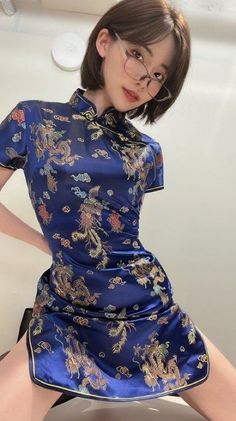 Woman in a blue cheongsam with dragon patterns and glasses posing indoors