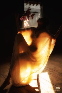Woman in sheer fabric dress with dramatic backlight holding flowers