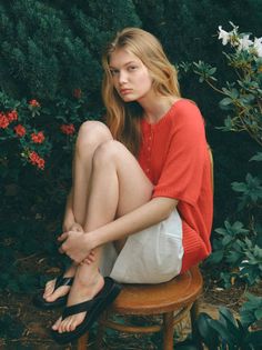 Blonde woman in a red top and white shorts sitting on a stool outdoors