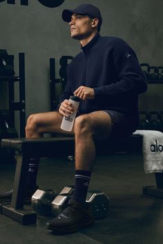 Man in athletic wear and a baseball cap sitting in a gym with a water bottle