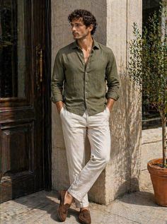 Man with curly hair wearing an olive shirt and white pants outdoors