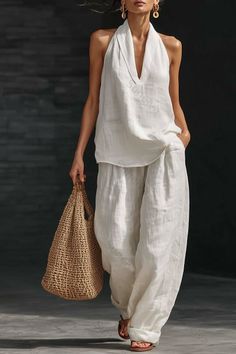 Woman in a white linen halter top and wide leg pants holding a straw bag