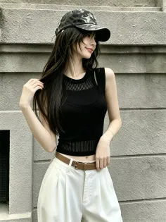 Woman in a black top and white pants with a camo cap, posing outdoors