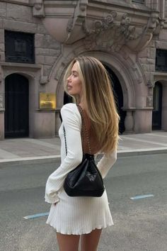 Woman with long hair in a white open-back dress and black handbag on a street