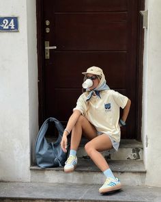 Person in casual attire sitting on steps outside a door, holding a cup