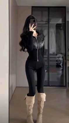 Woman in a black quilted jacket and beige boots taking a mirror selfie