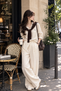 Woman in a striped shirt and wide leg pants holding coffee outside a cafe