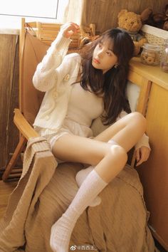 Woman in a white cardigan and shorts sitting indoors with soft lighting