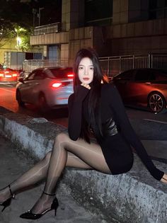 Woman in a black dress and sheer tights sitting on a curb at night